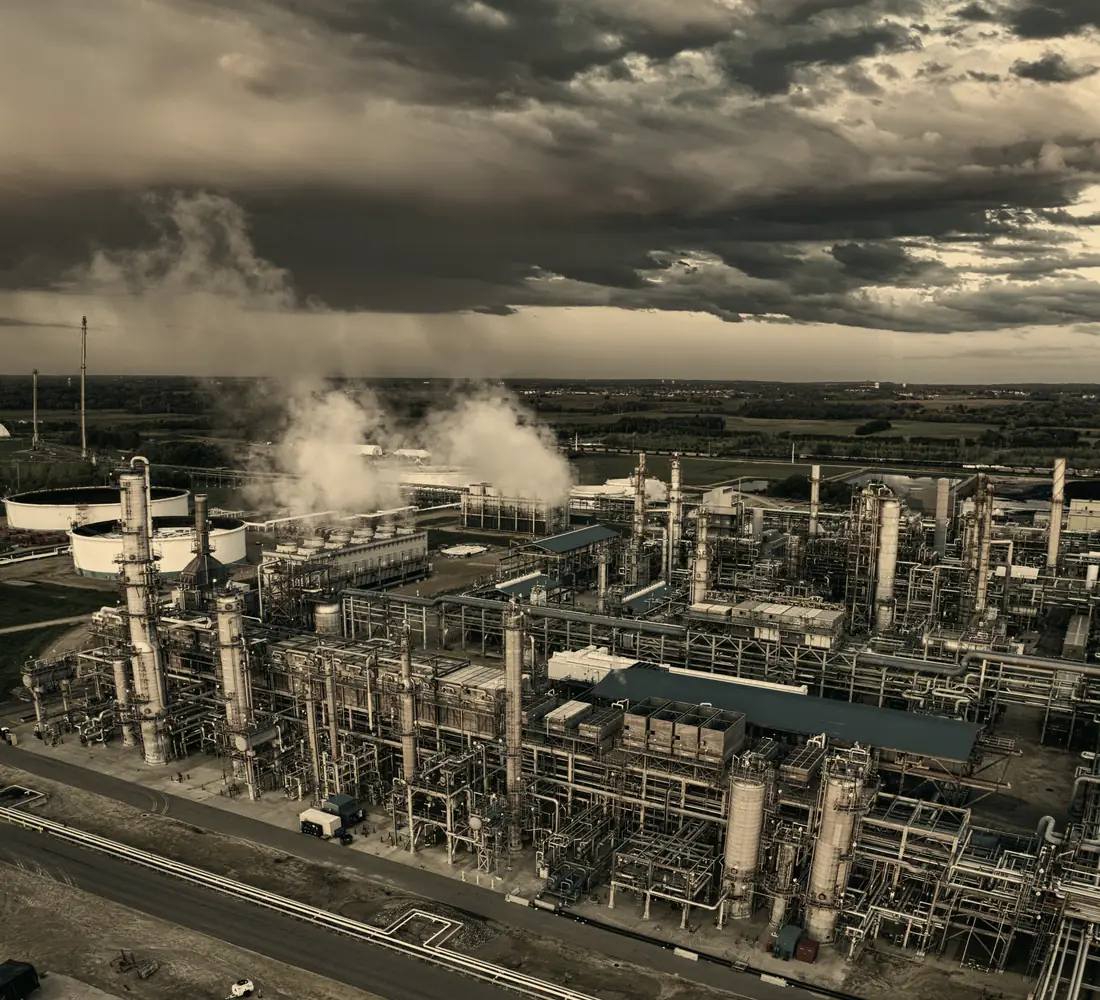 Complexo industrial ao entardecer, com chaminés e tubulações